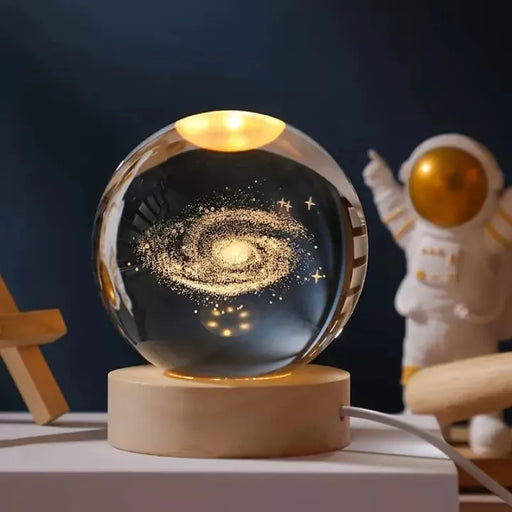 Glass ball with galaxy design on a wooden base, surrounded by decorative items.