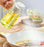 Person pouring oil from a bottle into a frying pan with a salad in the background