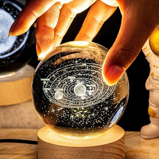 Glass sphere with solar system model on a wooden stand, held by a hand.